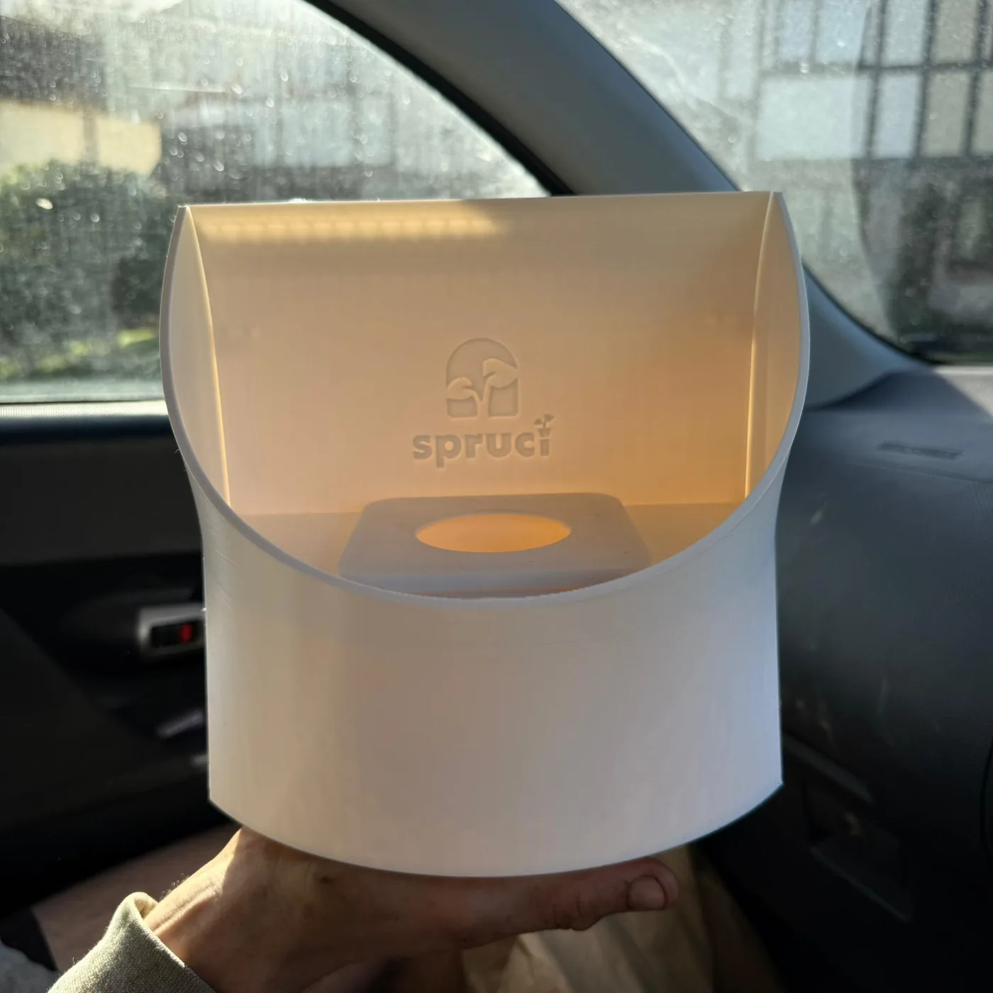 A white Spruci module held up in the light, the Spruci mark embossed into the shell