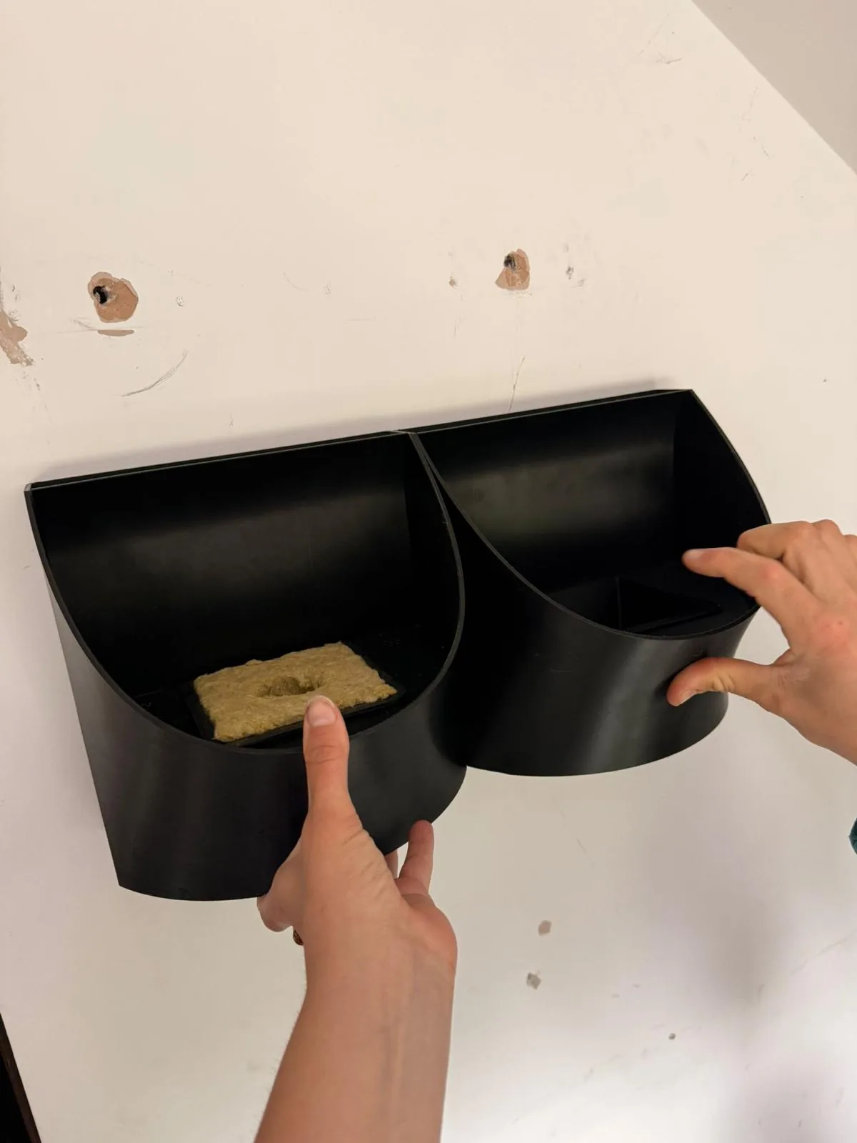 Two Spruci modules mounted side by side on a wall, a hand steadying the second one
