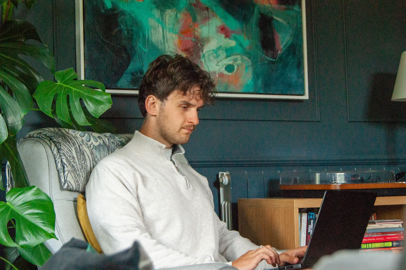 Ben Miller working on a laptop at home, an abstract painting on the wall behind him